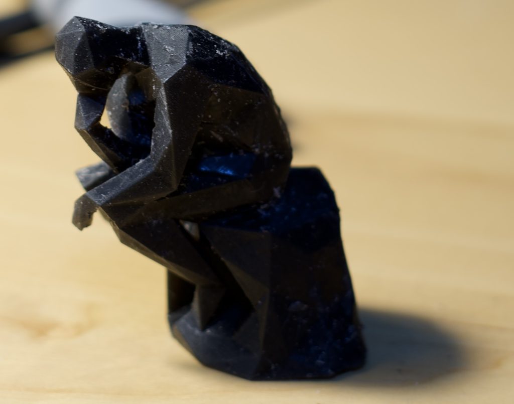 Rodin's The Thinker, in a low poly renditions, printed in black resin and displayed over a light wooden table